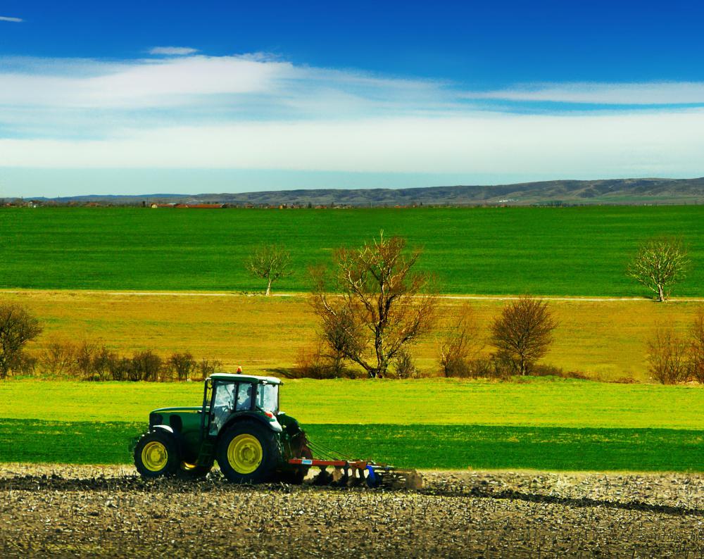 A farmer uses a tractor to pull a cultivator.