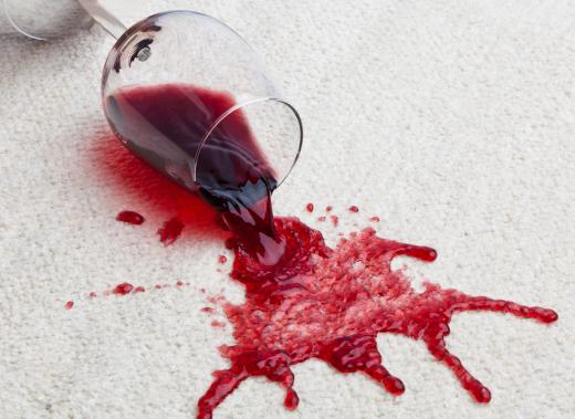 Glass of red wine spilled on a white carpet.